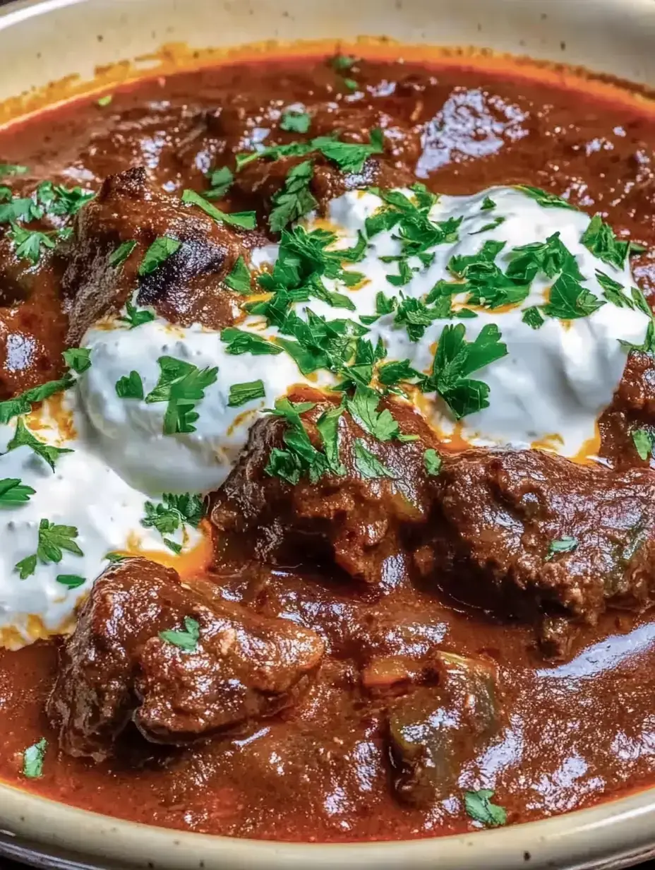 A rich dish of juicy meat in flavorful sauce, topped with fresh cilantro and a spoonful of yogurt.