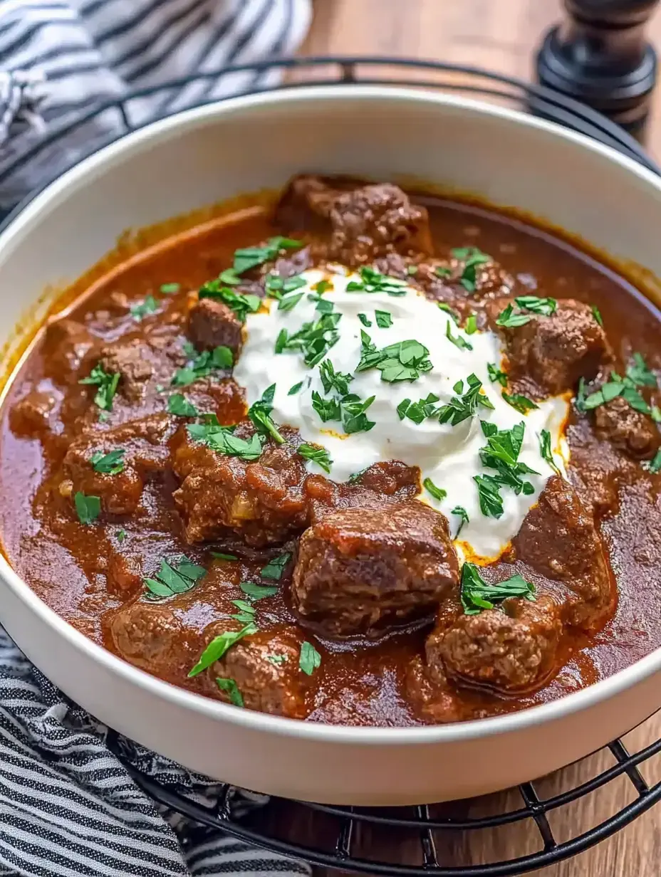 A plate of spiced beef stew, topped with fresh herbs and a swirl of sour cream.