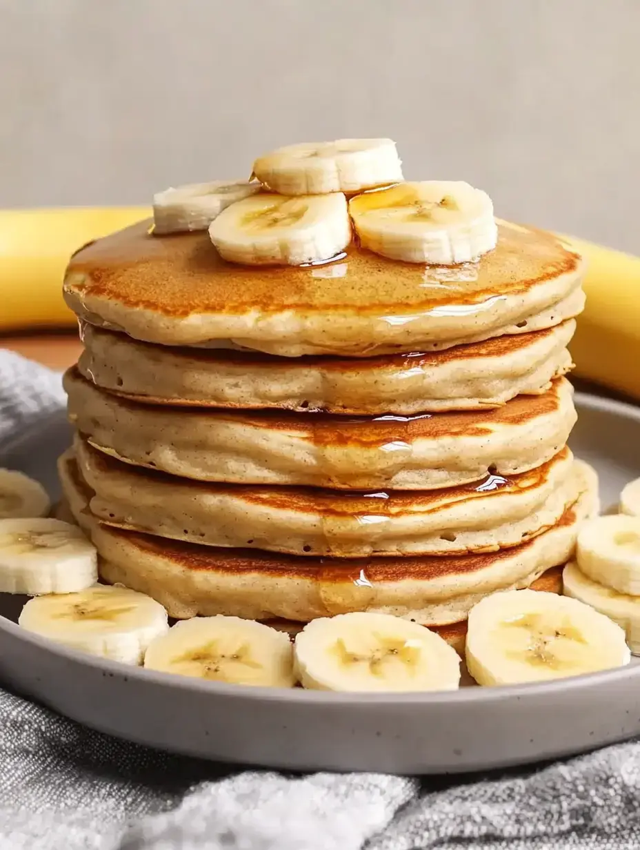 A stack of pancakes topped with banana slices and syrup on a plate.