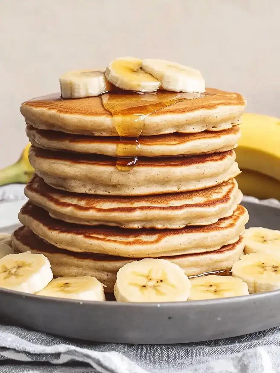 A stack of pancakes topped with banana slices and honey on a plate.