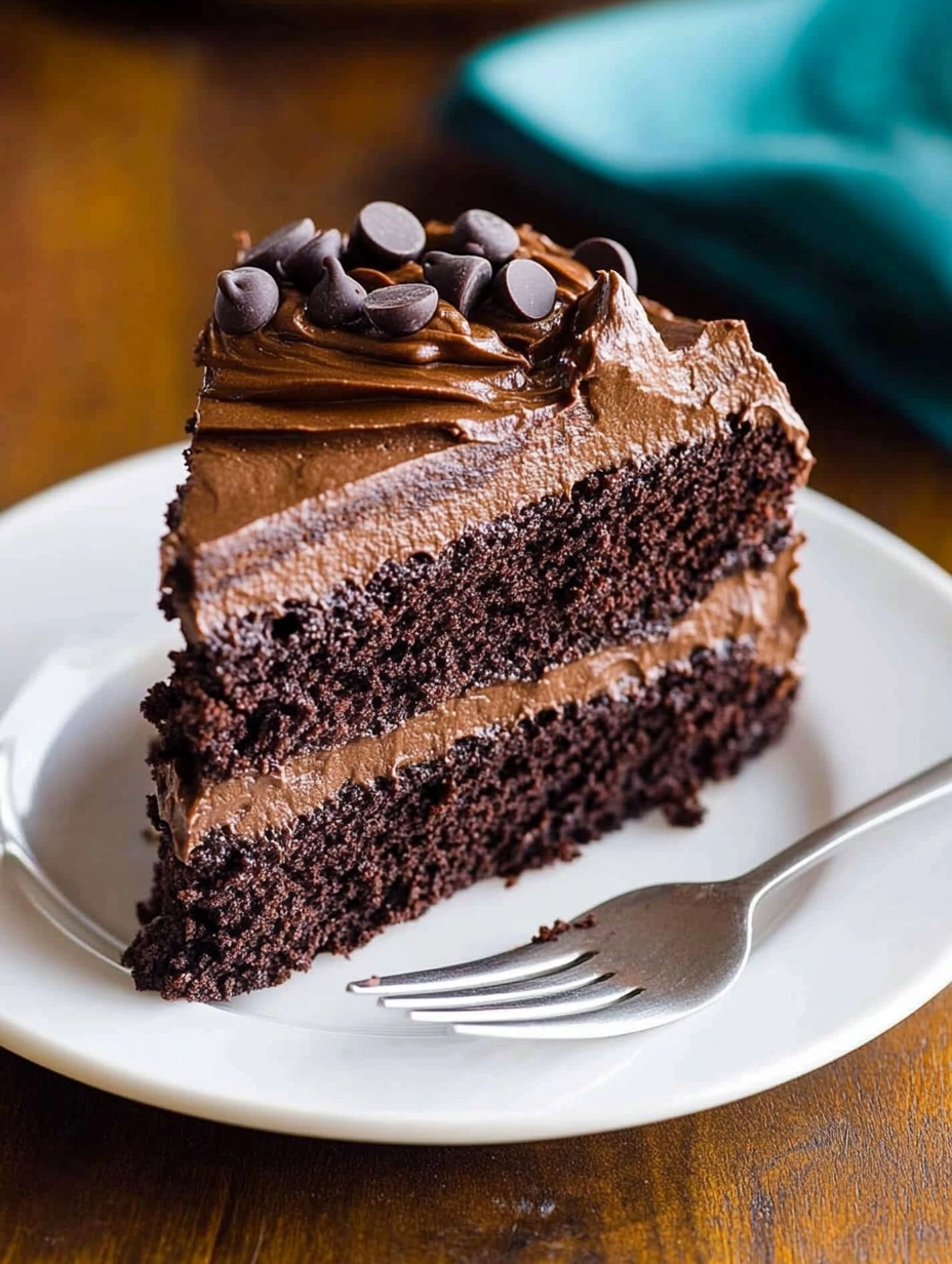 A slice of chocolate cake with chocolate chips on a white plate.