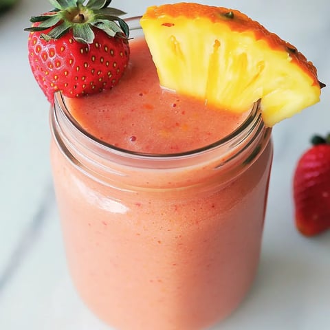 A glass of pink juice with a slice of pineapple on top.